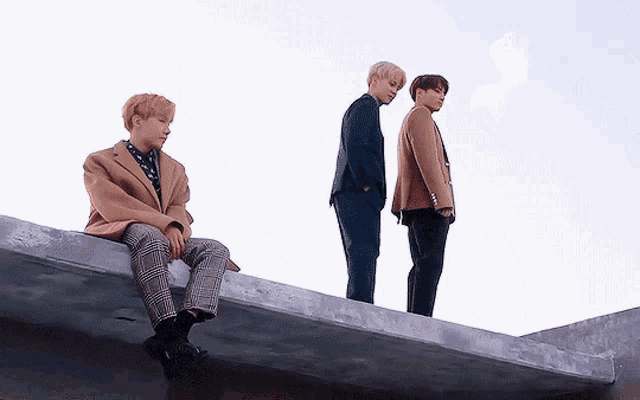 three men are standing on top of a building and one of them is sitting on a ledge .