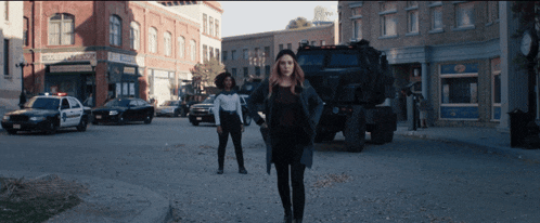 two women are walking down a street next to a police car