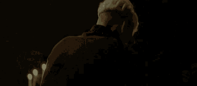a man with a shaved head stands in a dark room with candles behind him