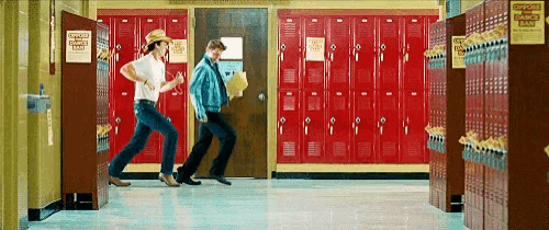 a couple of people are running in a hallway with red lockers .