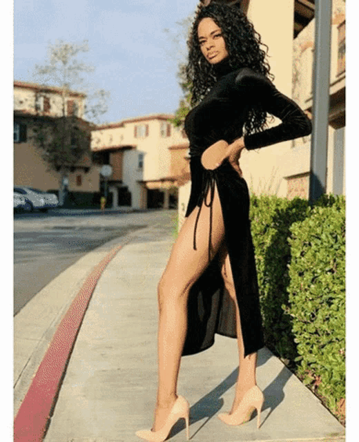 a woman in a black dress with a high slit on the sidewalk