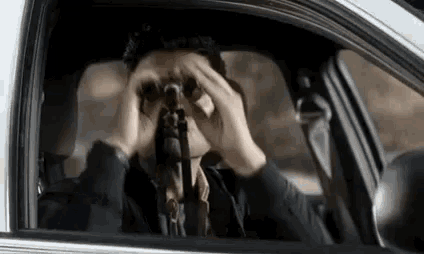 a man is looking through binoculars in a car .