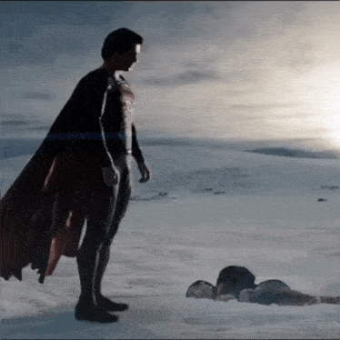 a man in a cape is standing next to a woman laying on the snow