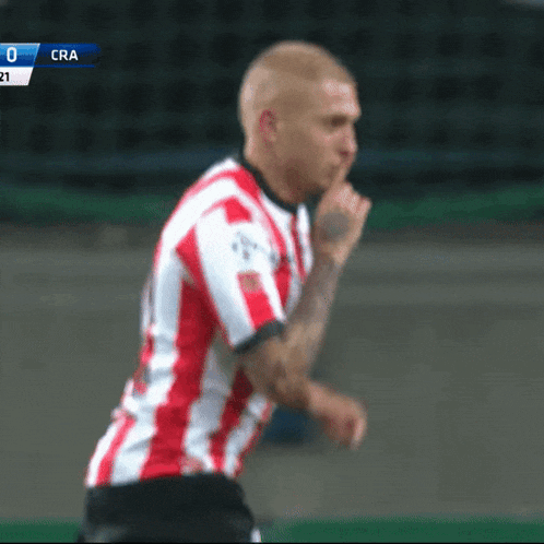 a soccer player in a red and white striped shirt holds his finger to his mouth during a game