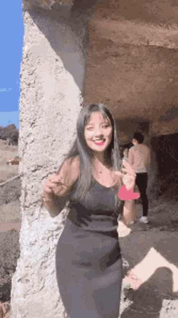 a woman in a black dress is standing next to a stone wall and smiling
