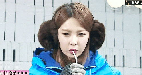 a woman wearing ear muffs and a blue jacket is holding a straw in her mouth