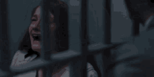a woman is crying in a jail cell with a man in the background