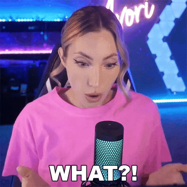 a woman in a pink shirt is talking into a microphone and says what