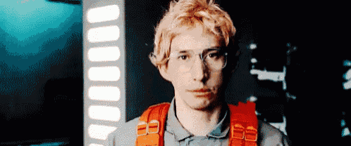 a man with blonde hair and glasses is wearing a gray shirt and orange harness .