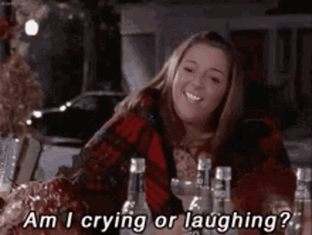 a woman is sitting at a table with bottles of wine and says am i crying or laughing ?