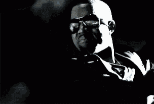 a man is wearing sunglasses and smoking a cigarette in a dark room .