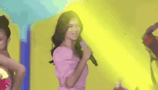 a woman in a pink dress is singing into a microphone while dancing on a stage .