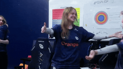 a woman in an orange shirt giving a thumbs up