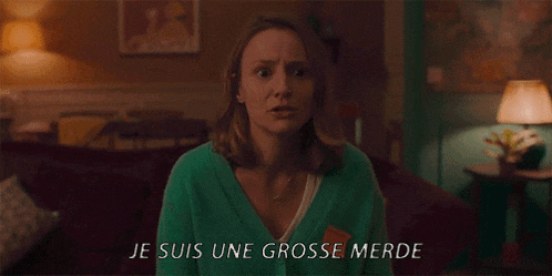a woman in a green sweater says je suis une grosse merde in a living room .