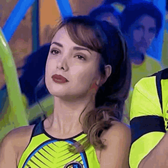 a woman in a yellow tank top is looking at the camera while standing in front of a crowd .