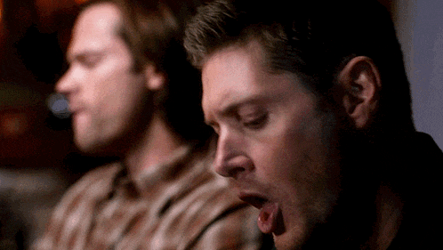 two men are sitting next to each other and one of them is yawning with his mouth open .