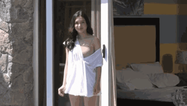 a woman in a white dress opens a sliding glass door to a bedroom