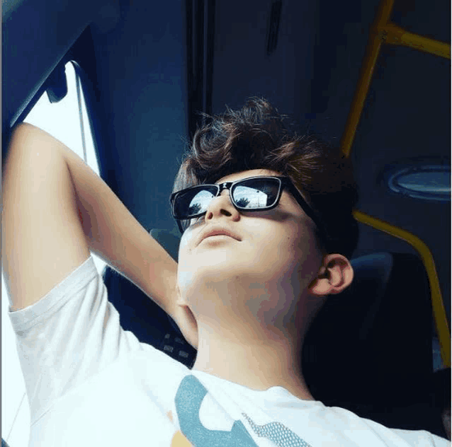 a young boy wearing sunglasses and a white shirt looks up at the sky