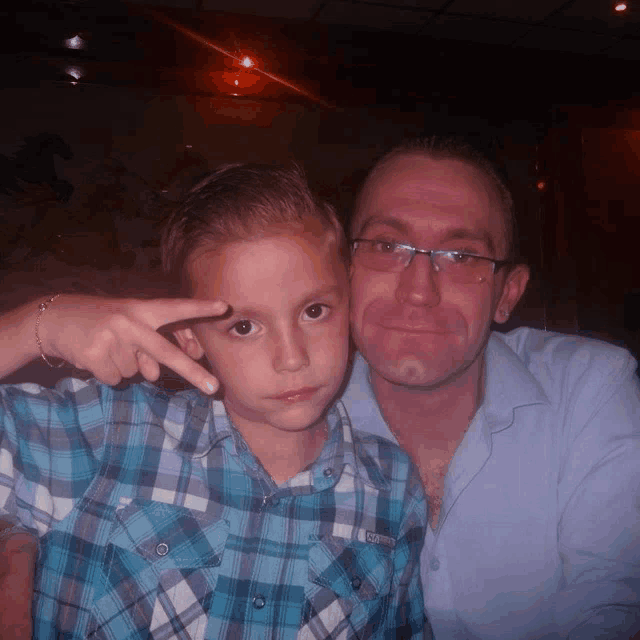 a man and a boy pose for a picture and the boy is wearing a plaid shirt that says superdry on it