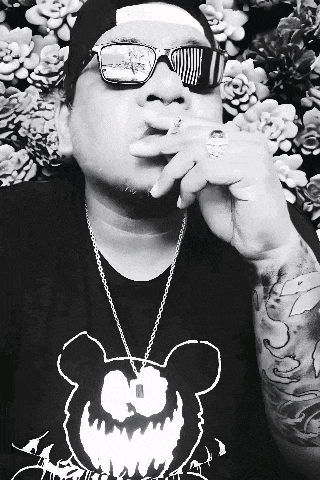 a man wearing sunglasses smoking a cigarette in front of a wall of succulents