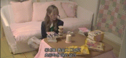 a woman is sitting at a table in a room with korean writing on the screen