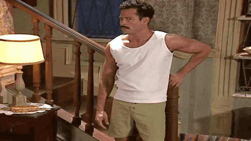 a man with a mustache wearing a white tank top is standing on a set of stairs