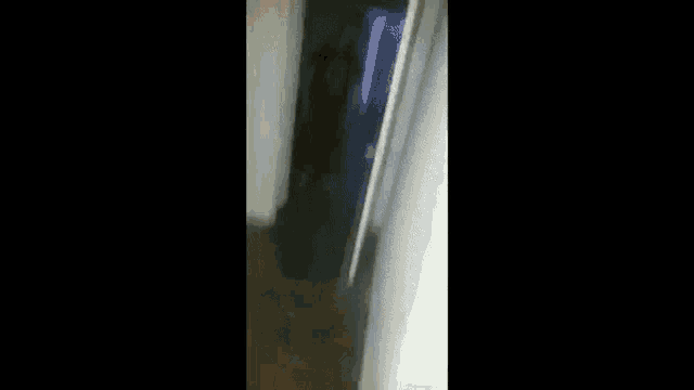 a person is walking down a hallway in a dark room with a light on the wall .
