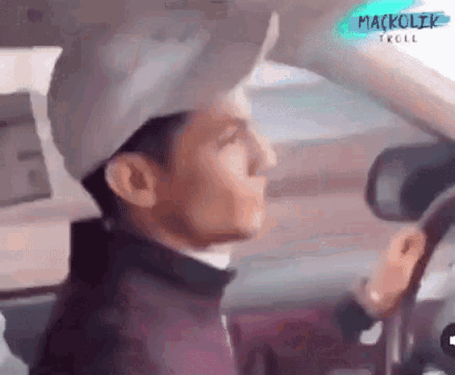 a man is driving a car with a white hat on his head .