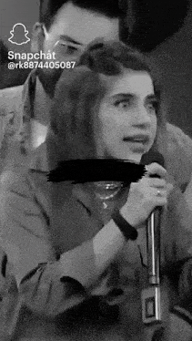 a woman is singing into a microphone while a man looks on .