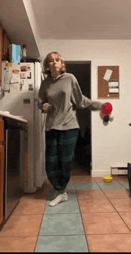 a woman is dancing in a kitchen with a ping pong paddle