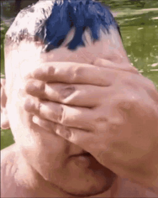 a man with blue hair covering his eyes with his hands