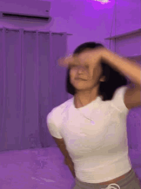 a woman is dancing in a room with purple lights and covering her face with her hand .