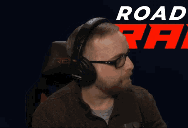 a man wearing headphones and glasses is sitting in front of a sign that says road rat