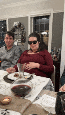 a woman wearing sunglasses sits at a table with a decanter of wine