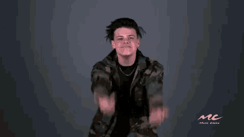 a man in a camouflage jacket is making a devil horns sign with his fingers .