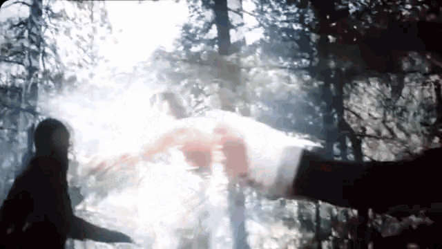 a person is standing in the woods with a sword in their hand and a person is flying through the air .