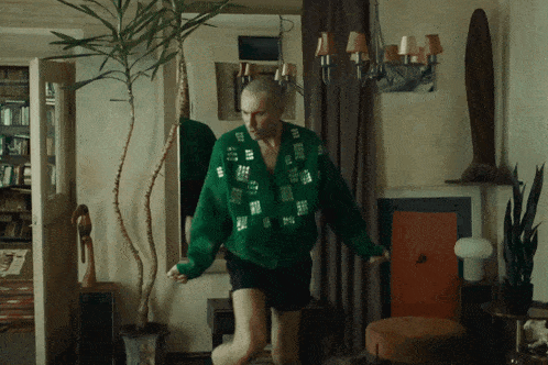 a man in a green sweater is dancing in front of a potted plant