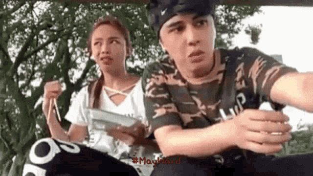 a man in a camouflage shirt is sitting next to a woman in a white shirt ..