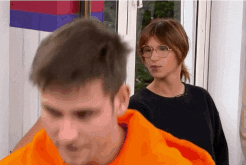 a man wearing an orange hoodie is standing next to a woman wearing glasses