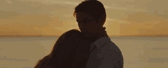 a man and a woman are hugging each other in front of the ocean at sunset