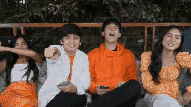 a group of people are sitting on a couch laughing and pointing at the camera