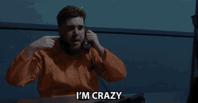 a man in an orange jumpsuit talking on a phone with the words i 'm crazy above him