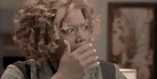 a woman with curly hair is covering her mouth with her hand in front of a painting .