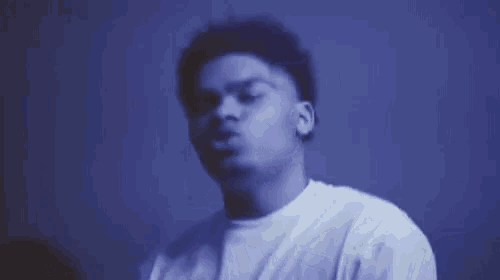 a young man is covering his nose with his hand while wearing a white t-shirt .