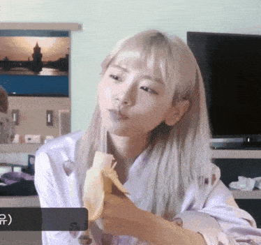 a woman with blonde hair is eating a banana in front of a television