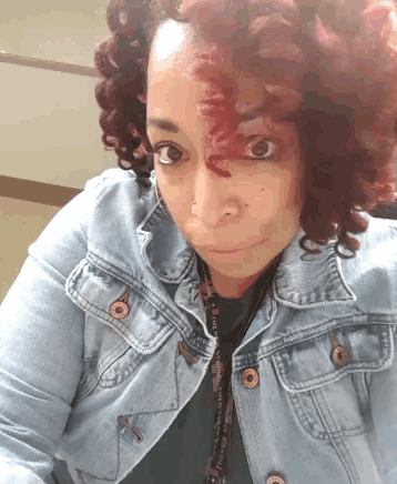 a woman with red curly hair is wearing a denim jacket and a lanyard that says ' nurse ' on it
