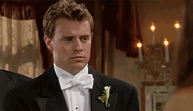 a man in a tuxedo and bow tie is standing in front of candles