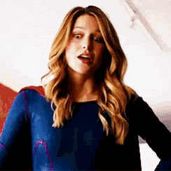 a woman in a blue superhero costume is standing with her hand on her hip .