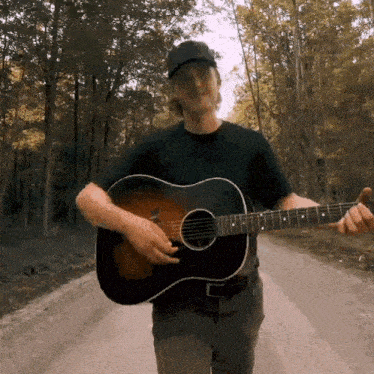 a man playing a guitar on a dirt road in the woods