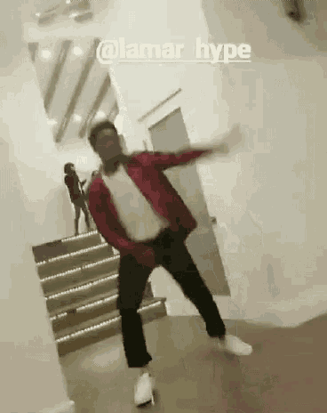 a man in a red jacket is dancing in a room with stairs in the background .